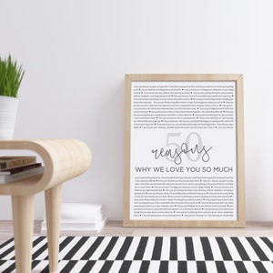 May include: A framed print with a white background and black text. The text reads "50 reasons why we love you so much". The print is on a wooden table with a black and white rug.