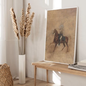 May include: A framed print of a vintage illustration depicting a person riding a horse. The print is on a beige background and features a brown horse with a rider wearing a blue and white uniform. The print is framed in a white frame.