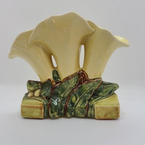 May include: A ceramic vase shaped like three white calla lilies with green leaves and brown accents. The vase is designed to hold flowers.