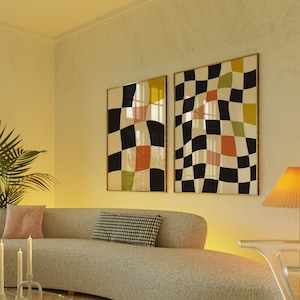 May include: A curved, light grey sofa with two cushions, one pink and one black and white checked, sits in a living room with a glass coffee table and a rug with a floral pattern. Two abstract paintings with black, white, yellow, and pink checked patterns hang on the wall.