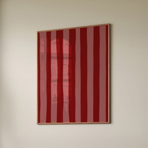 Puede incluir: Una impresión enmarcada de un patrón de rayas rojas y blancas con una imagen borrosa de una ventana y una vista al mar en el fondo.