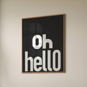 Puede incluir: Una impresión enmarcada en blanco y negro con el texto "oh hello" en letras blancas sobre un fondo negro.