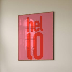 Peut inclure: Une affiche encadrée rose avec le mot "hello" en lettres rouges. Les lettres sont stylisées et ont un style rétro.