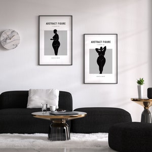 Pu&ograve; includere: Due stampe artistiche in bianco e nero incorniciate con la scritta "ABSTRACT FIGURE" e la silhouette di una donna. Le stampe sono appese a una parete bianca sopra un divano e un tavolino neri. Un orologio in marmo &egrave; sulla parete.