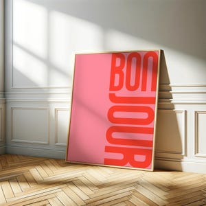 Pode incluir: Um p&ocirc;ster emoldurado rosa e vermelho com a palavra "BONJOUR" em letras vermelhas em negrito.
