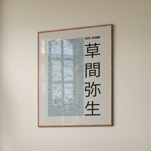 Puede incluir: Un póster enmarcado con un patrón de lunares azules y blancos y el texto "Yayoi Kusama" y "草間彌生" en negro.
