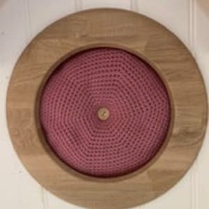 May include: A round wooden frame with a pink crocheted circle inside. The crocheted circle has a button in the center.
