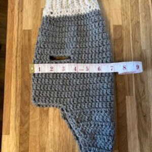 May include: Gray and white crocheted dog sweater with a hole for the leash. The sweater measures 9 inches across.