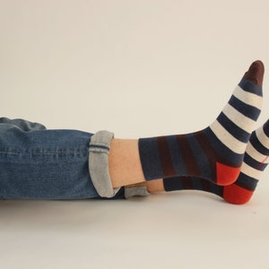 May include: A pair of striped socks with red, white and blue stripes. The socks are worn on a person's feet, with the legs of blue jeans visible.