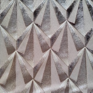 Op de afbeelding: Een close-up van een beige stof met een geometrisch patroon van overlappende driehoeken in tinten bruin en wit.