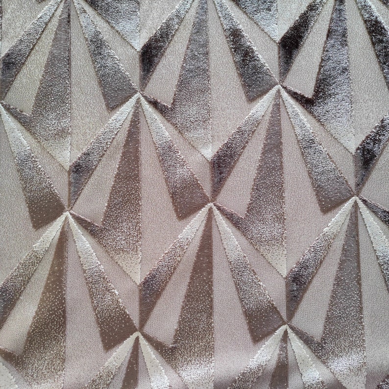 Op de afbeelding: Een close-up van een beige stof met een geometrisch patroon van overlappende driehoeken in tinten bruin en wit.