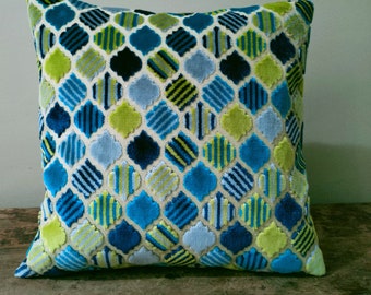 Puede incluir: Una almohada decorativa con un patrón geométrico en tonos de azul, verde y blanco. El patrón presenta un diseño repetitivo de cuatrifolios y rayas.