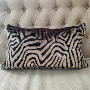 May include: A decorative cushion with a black and gold abstract pattern. The cushion is made of a soft, plush fabric.