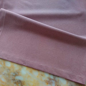 May include: A pink table runner with a textured surface and a stitched edge.