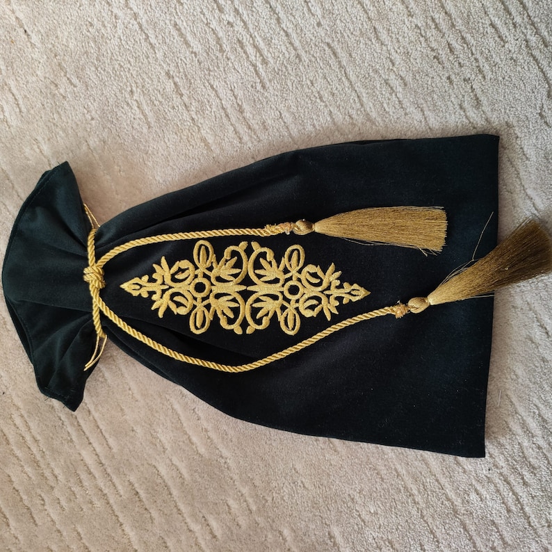 Puede incluir: Una bolsa de cord&oacute;n de terciopelo negro con bordados dorados y borlas. El bordado presenta un dise&ntilde;o floral.