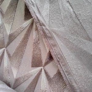 Op de afbeelding: Twee stukken stof met een geometrisch patroon. Het ene stuk is lichtbruin met een geometrisch patroon van driehoeken. Het andere stuk is lichtbeige met een textuur.