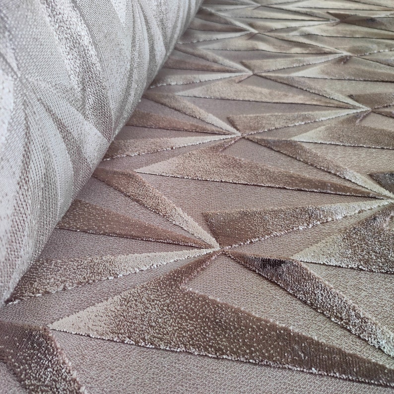 Op de afbeelding: Close-up van een beige tapijt met een geometrisch patroon van reli&euml;f driehoeken. Het tapijt heeft een zachte, pluche textuur.