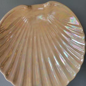 May include: A large, iridescent, pearlescent white ceramic seashell dish. The dish is shaped like a scallop shell with a smooth, rounded interior.