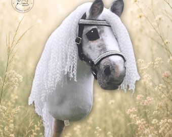 Può includere: Un cavallo giocattolo su bastone di colore bianco con una lunga criniera bianca riccia e una briglia nera con finiture argentate. La testa del cavallo è montata su un bastone di legno. Il testo include SMarti Horses e Handmade in Czech Republic.