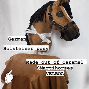 Op de afbeelding: Een bruin en wit Duits Holstein pony paardenhoofd gemaakt van caramel SmartIhorses Velboa stof. Het paard draagt een zwart halster en een wit lint.