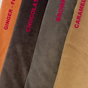 Puede incluir: Primer plano de muestras de tela en tonos naranja, marr&oacute;n y beige. Los colores est&aacute;n etiquetados con los nombres "Ginger - Fox", "Chocolate", "Brown" y "Caramel" en texto rojo. La tela parece suave y afelpada.