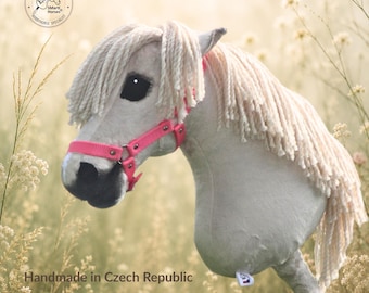 Può includere: Un cavallo giocattolo in peluche con manto color crema chiaro, lunga criniera in filo bianco e muso grigio scuro. Il cavallo presenta una cavezza in nylon rosa acceso con fibbie in metallo argentato ed è montato su un manico in legno.