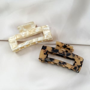 May include: Two hair clips, one white with a marbled pattern and one brown with a tortoiseshell pattern.