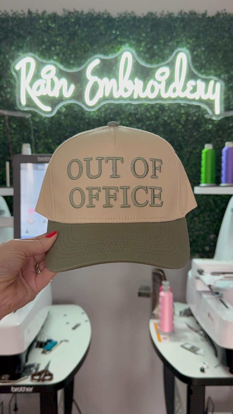 May include: A beige and green baseball cap with the text "OUT OF OFFICE" embroidered in white on the front.