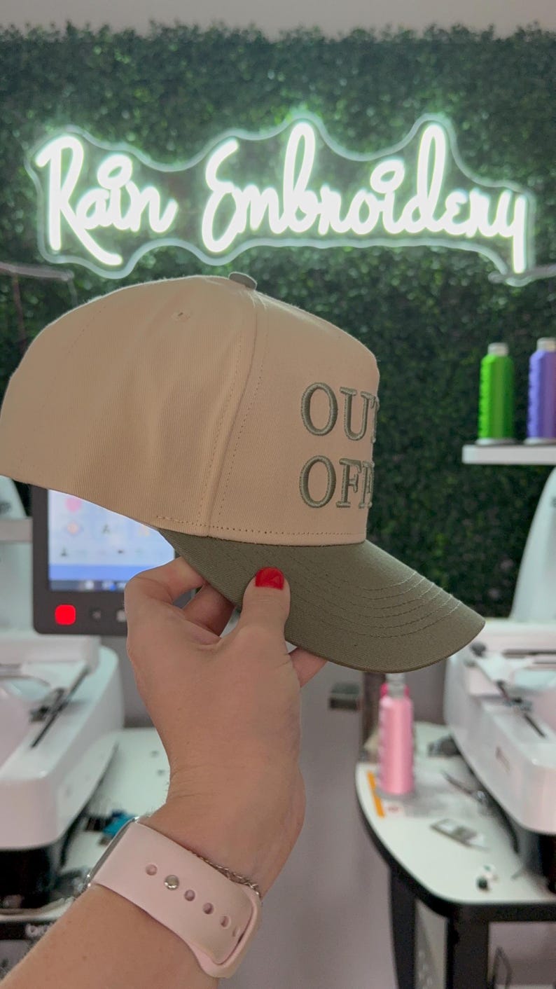 May include: A beige and green baseball cap with the text "OUT OF OFFICE" embroidered on the front.