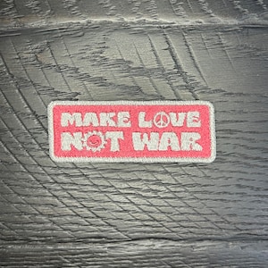 May include: Red embroidered patch with white text that reads "Make Love Not War" with a peace sign and a smiley face with a gear in the middle.