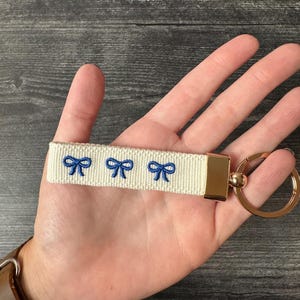 May include: A white key chain with three blue bow designs and a gold metal key ring.