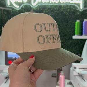 May include: A beige and green baseball cap with the text "OUT OF OFFICE" embroidered in green on the front.