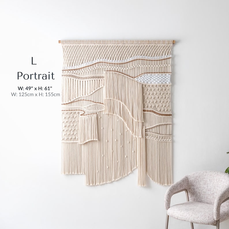 Large portrait-oriented macrame wall hanging measuring 49 by 61 inches. This long vertical tapestry showcases deep textured patterns, thick woven lines, and long, elegant fringe hanging above a modern chair.