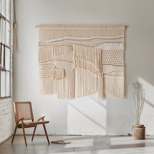 May include: A large, beige macrame wall hanging with a woven pattern. The wall hanging is made of natural fibers and has a bohemian style.