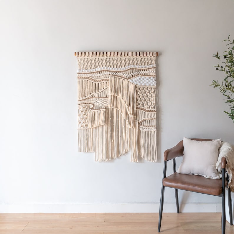May include: A large, beige macrame wall hanging with a woven pattern. The hanging is made of natural fibers and has a rustic, bohemian style.