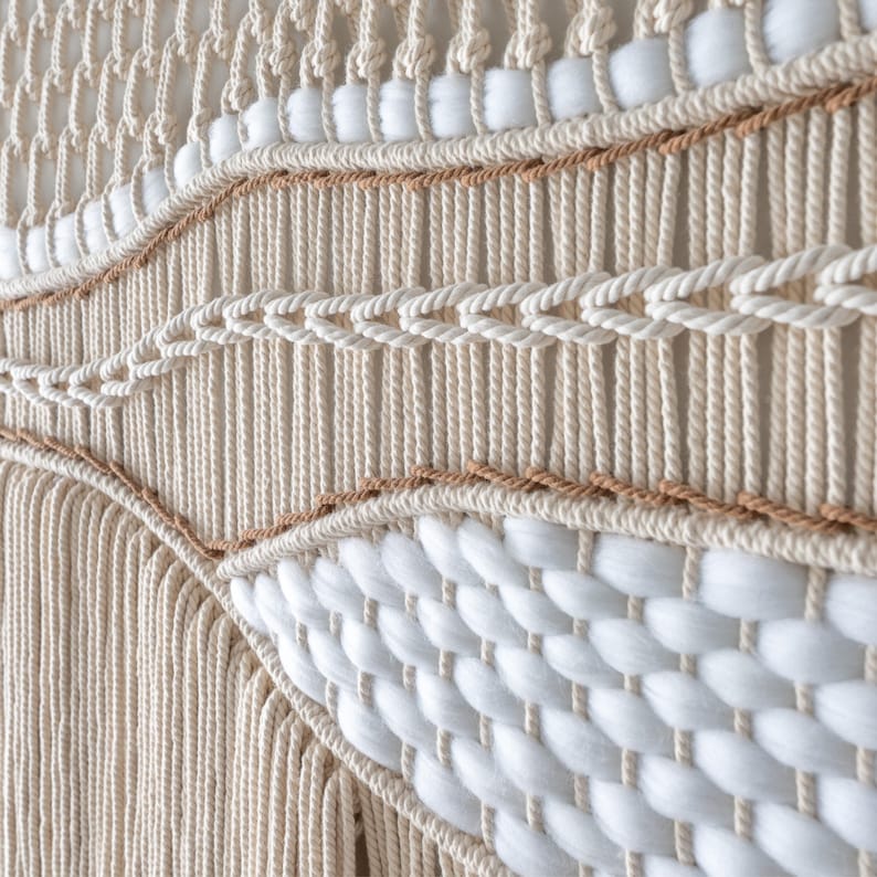 Close-up detail of a handmade macrame wall hanging showing mixed textures. Thick, fluffy white wool is woven between rows of tightly knotted natural beige cotton cord, creating a dynamic, wavy bohemian pattern.