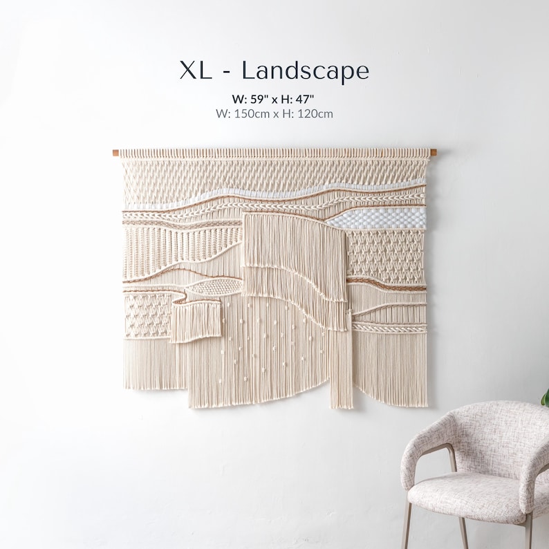 Extra large landscape macrame wall hanging measuring 59 by 47 inches. A woman is standing next to the massive fiber art piece, touching the edge to show scale. The tapestry features rich, 3D textures and varying lengths of cotton cord.