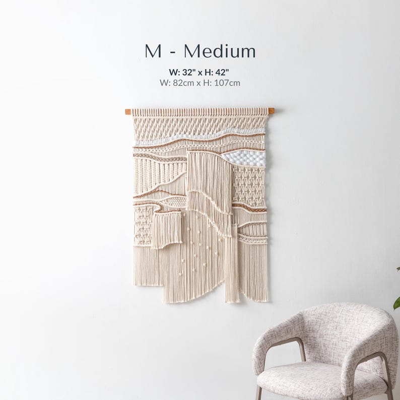 Medium handmade macrame wall hanging measuring 32 by 42 inches. The tapestry features intricate, textured knotting, a wave pattern, and layered fringe, displayed against a clean white wall above a modern textured chair.