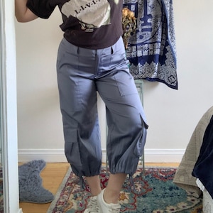 May include: A person wearing a black t-shirt with a white graphic that says "L.I.V.I.N."  The person is also wearing a floral print bucket hat and blue cargo pants.