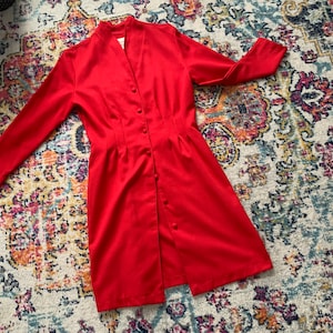 May include: A red button-up dress with long sleeves. The dress has a v-neck and a fitted waist.