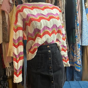 Puede incluir: Un maniqu&iacute; exhibe un su&eacute;ter colorido y una falda de mezclilla. El su&eacute;ter presenta un patr&oacute;n de ondas en blanco, rosa, naranja y verde. La falda es de mezclilla de lavado oscuro con botones frontales y dos bolsillos delanteros. Ropa.
