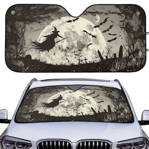 May include: A black and white Halloween-themed car sunshade featuring a witch on a broomstick flying in front of a full moon, with bats, trees, and tombstones. The sunshade is displayed on a white car.