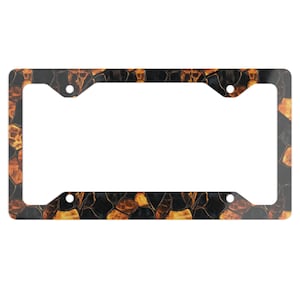 May include: A rectangular license plate frame with a black and gold abstract pattern. The frame has four mounting holes and a white interior space for the license plate. The pattern has a mosaic-like appearance.