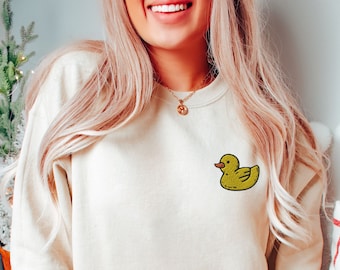 May include: A cream-colored sweatshirt with a yellow rubber ducky embroidered on the left chest.