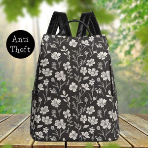 May include: A black backpack with a white floral pattern. The backpack has a zippered pocket on the front and adjustable straps.