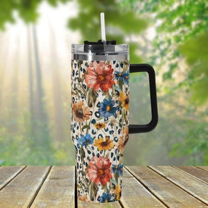 May include: A stainless steel tumbler with a floral and leopard print design. The tumbler has a black lid and handle and a clear straw.