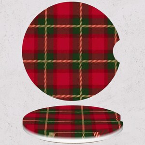 May include: Two car coasters with a red, green, and gold plaid pattern. One coaster is upright, and the other is lying flat. The coasters have a circular shape with a small notch on one side.