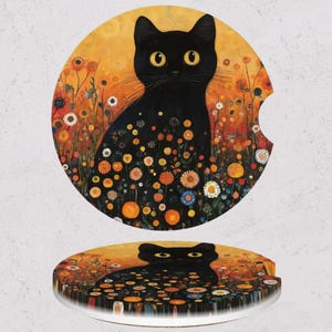 May include: Two round car coasters featuring a black cat with yellow eyes, surrounded by colorful flowers. The background is a warm orange hue. One coaster has a cutout for a car cup holder.