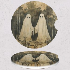 May include: Two round car coasters with a spooky forest scene. The coasters feature two white ghosts holding hands in a dark forest. The background is a mix of dark and light shades, creating a vintage, Halloween-themed design.