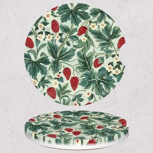 May include: Two round car coasters with a strawberry and leaf pattern. The design features red strawberries, green leaves, and white flowers on a light green background. The coasters are made of a durable material.